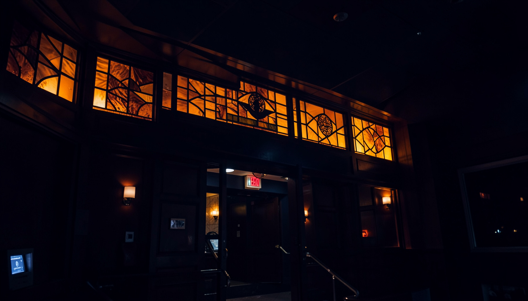 Atmospheric dark theater lobby with amber accent lighting along the marquee, deep navy shadows, and warm glowing signage